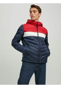 Padded bunda s kapucí, která má červený a bílý horizontální pruh přes hrudník, navy modrou barvu a zipový uzávěr.
