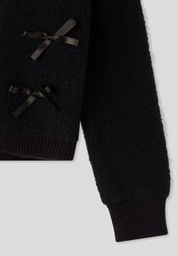 Maglione nero lavorato a maglia con superficie testurizzata, polsini a coste e due accenti in nastro nero sul davanti. Materiale morbido.