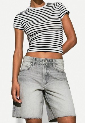 Persoon die een zwart-wit gestreept kort mouw crop top en lichtgrijze, hooggetailleerde denim shorts met rafelige zoom draagt.