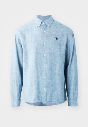 Light blue button-up shirt in a textured fabric. Features a collar, long sleeves, and a small dark logo on the chest.