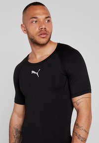 Svart kortermet treningsskjorte laget av elastisk materiale, med en sølv Puma-logo på brystet og en tettsittende design.