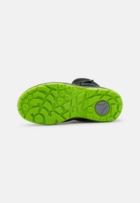 Scarpa sportiva nera con suola in gomma verde testurizzata, caratterizzata da un motivo di battistrada unico e un accento grigio del logo vicino al tallone.