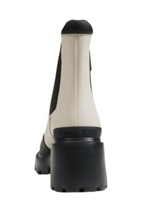 Béžová kotníková bota s černými elastickými stranami, masivní podrážkou a matným povrchem. Na patě je vyraženo "TOMMY JEANS".