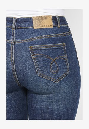 Dark blue denim jeans with a visible logo patch on the back waistband and detailed stitching on the back pockets.