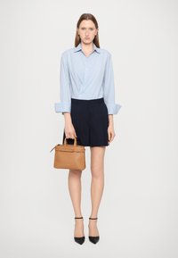 Light blue striped button-up shirt, navy shorts, black pointed shoes, and a tan handbag with a top handle and zipper.