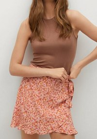 Een bruine mouwloze top gecombineerd met een mini-jurk in een roze bloemenpatroon met een gerimpelde zoom en een geknoopt detail aan de zijkant.