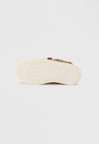 Mitmevärviline king, millel on mustriga pealis, tekstureeritud kreemjas kummist tald ja ümmargune haardedisain. Rõhutatakse kaunist logot.