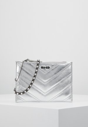 Zilverkleurige metallic clutch met doorgestikt chevron-patroon, NA-KD-logo, ritssluiting en een zilveren kettingriem die over de voorkant hangt.