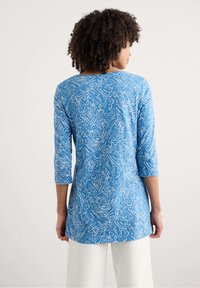 Blauwe tuniek met een wit bloem- en abstract patroon, 3/4 mouwen, ronde halslijn en een losse pasvorm. Gemaakt van lichtgewicht stof.