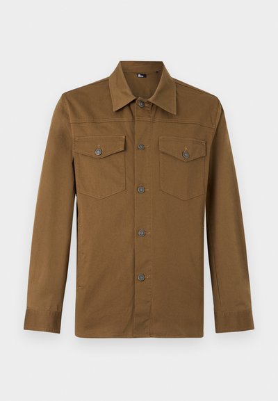 Καφέ πουκάμισο με μακριά μανίκια, κουμπιά, μυτερό γιακά και δύο τσεπάκια στο στήθος με κουμπιά, απεικονίζεται σε απλό φωτεινό φόντο.