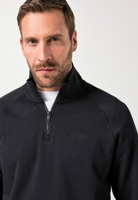 Maglione zip-up nero con colletto alto e logo ricamato "JP1880" sul davanti. Tessuto morbido, design casual e vestibilità regolare.