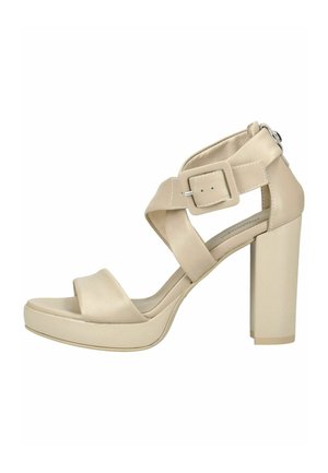 Sandalia de tacón alto beige con tiras anchas entrecruzadas, cierre con hebilla grande y tacón grueso, sobre un fondo blanco.