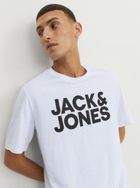 Balts kokvilnas T-krekls ar lieliem melniem burtiem "JACK & JONES", kas izdrukāts uz priekšpuses. Īsas piedurknes un klasiskā apaļā kakla dizains.