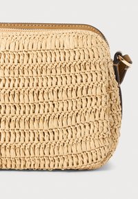 Borsa a tracolla in paglia intrecciata di un beige chiaro, con superficie texturizzata, chiusura a zip semplice e dettagli in pelle marrone. Design compatto e leggero.