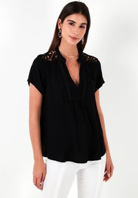 Blusa nera con scollo a V, maniche corte, dettagli in pizzo sulle spalle e rifiniture decorative lungo il collo. Tessuto morbido con vestibilità comoda.