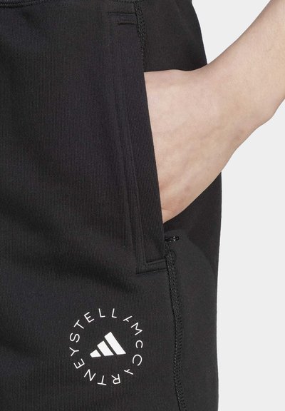 Melni sporta bikses ar rāvējslēdzēja kabatu, ar aplīgu baltu logotipu un izteiksmīgu trīs svītru dizainu, izgatavotas no mīksta, elastīga auduma.