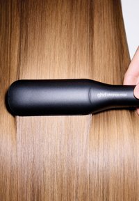 GHD Chronos Max stijltang met een sleek zwarte handgreep boven glanzend, steil blond haar, dat de zachte textuur en egale glans laat zien.