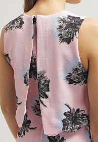 Hihaton kukkakuosisepäroinen paita vaaleanpunaisessa sävyssä, jossa on pehmeä, rakenteellinen kangas, takana avainreikäyksityiskohta sekä mustia ja sinisiä kukkapainatuksia.