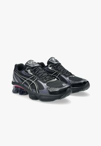 Scarpe da ginnastica nere con tomaia in mesh, dettagli metallici argentati e suola spessa con un elemento di ammortizzazione in gel ben visibile.