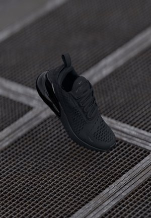 Black Nike Air Max sneaker floating above metal grid flooring with diagonal support bars in a dark, industrial setting.