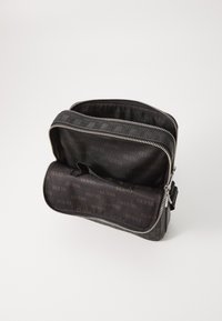 Fekete nylon táska textúrált mintával, dupla cipzárral és belső részén ismétlődő "GUESS" logó mintázattal. Kompakt, állítható pánttal.
