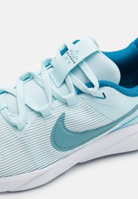 Baskets de sport bleu clair avec une tige texturée, des accents bleus coordonnés et une semelle blanche. Présente un logo en forme de virgule et des éléments de design à rainures.