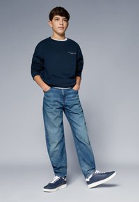 Felpa navy, jeans in denim blu e sneakers navy. Vestibilità casual con polsini e orli a coste, con un piccolo logo sulla felpa.