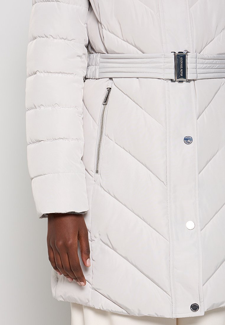 Jasnoszara kurtka puchowa z paskiem w talii, z haftem w zygzak, zamykanymi kieszeniami po bokach oraz zapięciem na zatrzask.