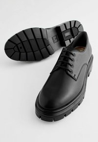 Scarpe da uomo in pelle nera, con punta arrotondata, design con lacci e suola in gomma spessa caratterizzata da un motivo di battistrada testurizzato.