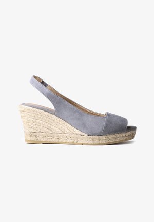 Sandalia de cuña con tiras traseras de ante gris, punta abierta y plataforma de yute trenzado, vista lateral sobre fondo blanco.