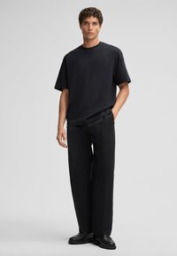 Schwarzes kurzärmliges T-Shirt, lockere Passform, aus Baumwolle, kombiniert mit schwarzer, maßgeschneiderter Hose, die eine glatte Textur und minimalistisches Design aufweist.