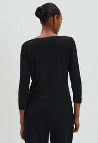 Haut noir à manches longues avec un col large, texture lisse, design ajusté et coupe droite à la taille, présenté de dos.