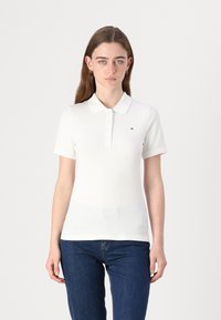 Valge polo särk krae ja viie nööbiga kinni. Omab lühikesi varrukaid ja väikest logo vasakul rinnal. Siledast kootud kangast.