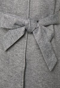 Szara dzianinowa tkanina z wiązanym paskiem zakończonym kokardą. Materiał ma miękką fakturę i subtelny wzór na całej powierzchni.