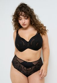 Reggiseno nero in pizzo con ferretti, caratterizzato da ricami floreali, bordi ondulati e un gancetto centrale, abbinato a mutandine alte in vita con dettagli in rete.