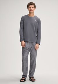 Grå langærmet skjorte i blødt stof. Grå mønstrede pyjamabukser med geometrisk design. Sorte slides på fødderne. Enkel, afslappet pasform.