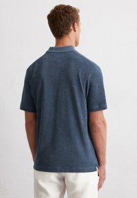 Donkerblauwe polo-shirt met korte mouwen en een platte kraag, gemaakt van een structuurstof. Zijsplitten aan de zoom voegen detail toe aan het ontwerp.