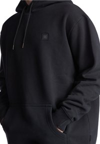 Haut à capuche noir en tissu mélangé coton, avec une poche kangourou, un capuchon avec cordon de serrage et un petit écusson logo sur la poitrine.