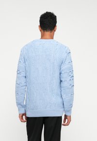 Ανάλαφρος μπλε πουλόβερ από πλέξη, μ�ε περίπλοκα υφασμάτινα μοτίβα, διαθέτει στρογγυλή λαιμόκοψη και ζώνες με ραφή στο κάτω μέρος και στα μανίκια.