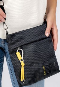 Borsa a tracolla nera in tessuto con zip sulla parte superiore, dettaglio giallo con clip e logo embossato. Forma rettangolare strutturata.