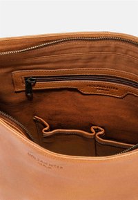 Brown leather bag interior featuring a zippered pocket, two compartments, and embossed "HOLZRICHTER" label on a textured fabric background.