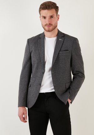 Gray tailored blazer with a textured fabric, single chest pocket, two front pockets, and two buttons. Worn over a white t-shirt and black pants.