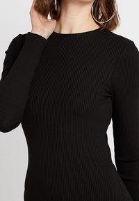 Schwarzes, geripptes Langarmoberteil mit taillierter Passform und rundem Halsausschnitt, aus dehnbarem Stoff mit glatter Textur.