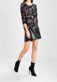 Blusa con motivo floreale di colore navy con maniche a tre quarti, abbinata a una mini gonna nera lucida. La modella indossa stivali neri alla caviglia.