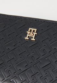 Svart teksturert lærpung med et preget geometrisk mønster og en gull logo plate. Strømlinjeformet design med bemerkelsesverdig detaljering.