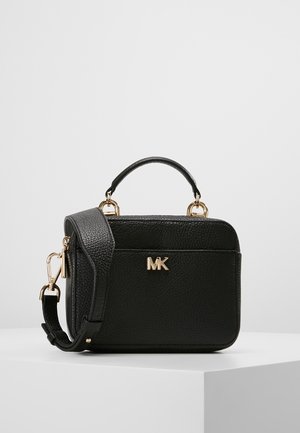 Sac bandoulière en cuir noir avec poignée supérieure, ferrures dorées et logo "MK" sur le devant, présenté sur un socle blanc.