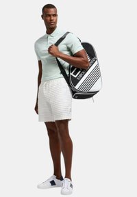 Mochila en blanco y negro con diseño a rayas, polo ligero en verde menta, pantalones cortos blancos con textura y zapatillas blancas con acentos azules.