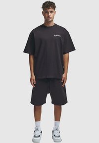 Camiseta negra de corte oversize con un sutil logo en el frente, combinada con unos pantalones cortos negros a juego. Llevada con zapatillas deportivas blancas y calcetines hasta la caña.