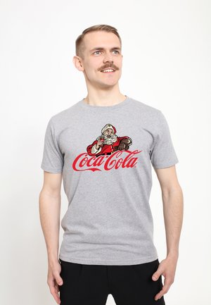 Man wearing gray t-shirt with vintage Santa holding a Coca-Cola bottle above the red Coca-Cola logo, standing against white background.