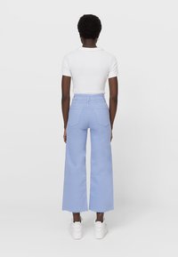 Pantalones vaqueros anchos de color azul claro con una cintura alta, dobladillo deshilachado y dos bolsillos traseros, combinados con una camiseta blanca ajustada. Diseño casual.